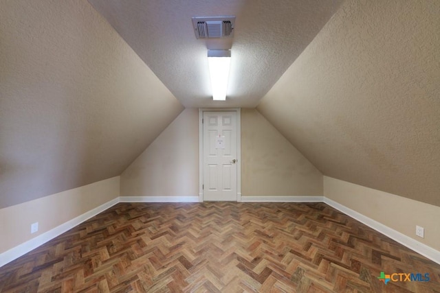 additional living space featuring dark parquet flooring, vaulted ceiling, and a textured ceiling