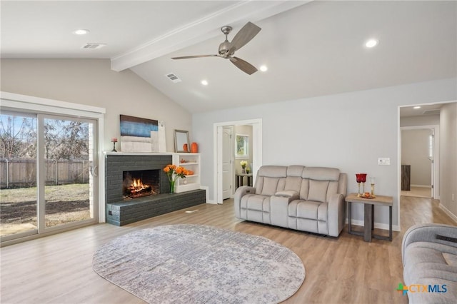 living room featuring vaulted ceiling with beams, light hardwood / wood-style flooring, a brick fireplace, and ceiling fan