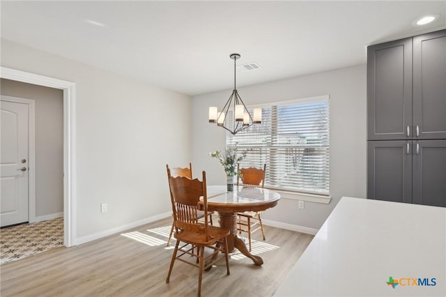 dining area featuring light wood finished floors, a notable chandelier, baseboards, and visible vents
