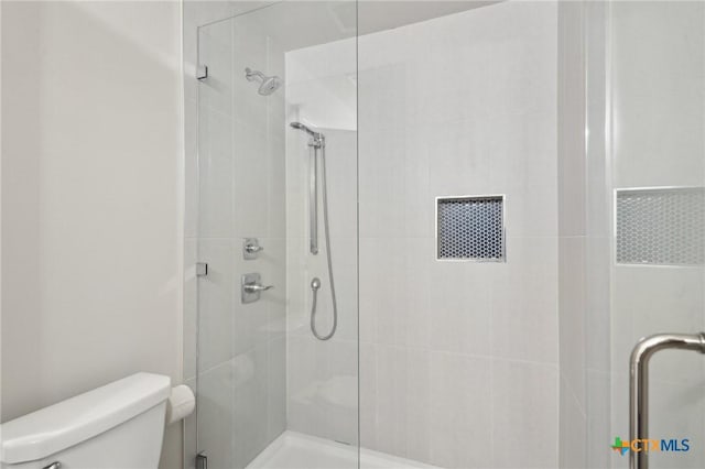 bathroom featuring a shower with shower door and toilet