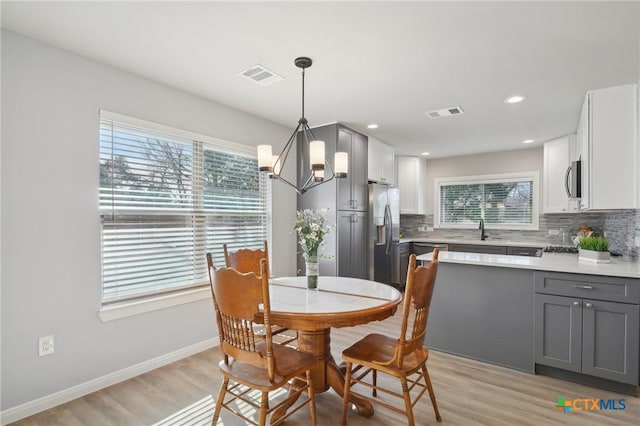 dining area featuring an inviting chandelier, sink, light hardwood / wood-style flooring, and a healthy amount of sunlight