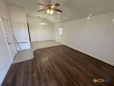 unfurnished room featuring dark hardwood / wood-style floors, ceiling fan with notable chandelier, and vaulted ceiling