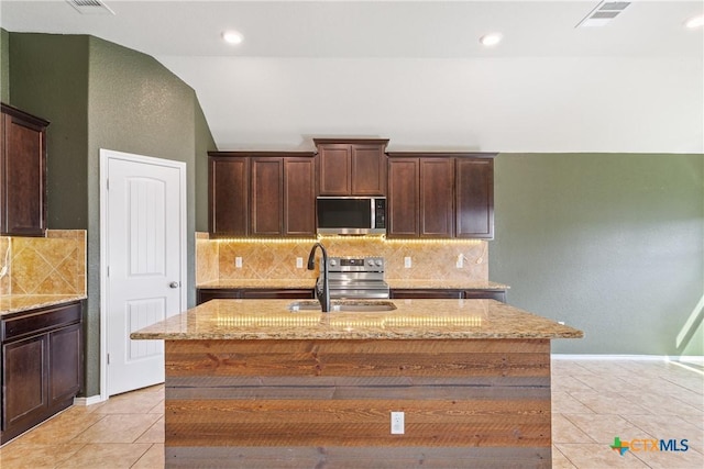 4004 Brookhaven Dr, Temple, TX 76504 - kitchen featuring stainless steel appliances, light stone counters, dark brown cabinetry, a kitchen island with sink, and light tile patterned floors