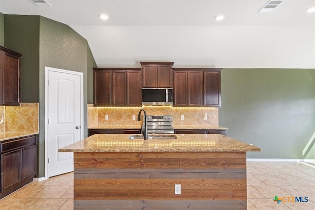 kitchen with dark brown cabinets, light stone countertops, a sink, light tile patterned floors, and stainless steel appliances