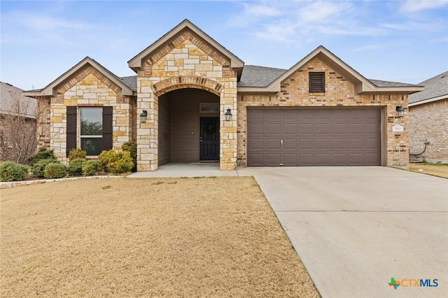 french country home with stone siding, concrete driveway, an attached garage, and a shingled roof