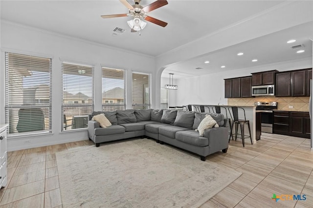 living room with crown molding, a ceiling fan, visible vents, and arched walkways