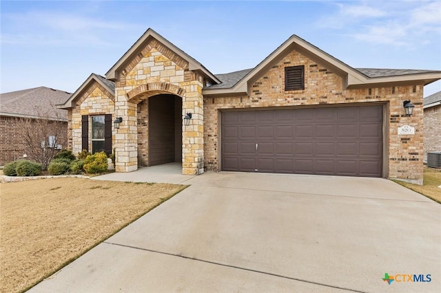 french country style house with brick siding, an attached garage, a shingled roof, stone siding, and driveway