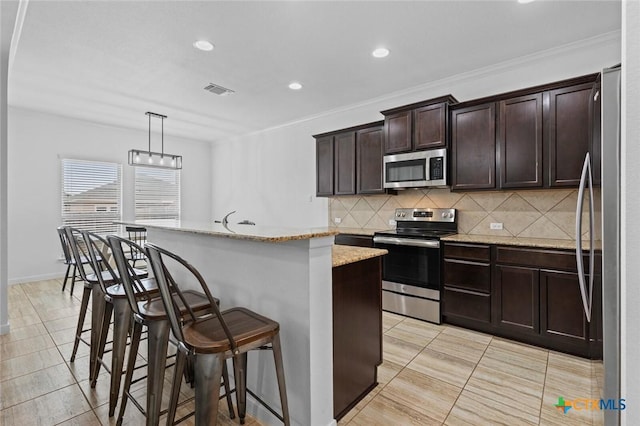 kitchen with a breakfast bar area, a kitchen island with sink, stainless steel appliances, decorative backsplash, and dark brown cabinetry