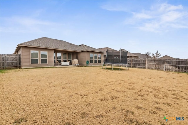 back of house with a fenced backyard, a trampoline, and roof with shingles