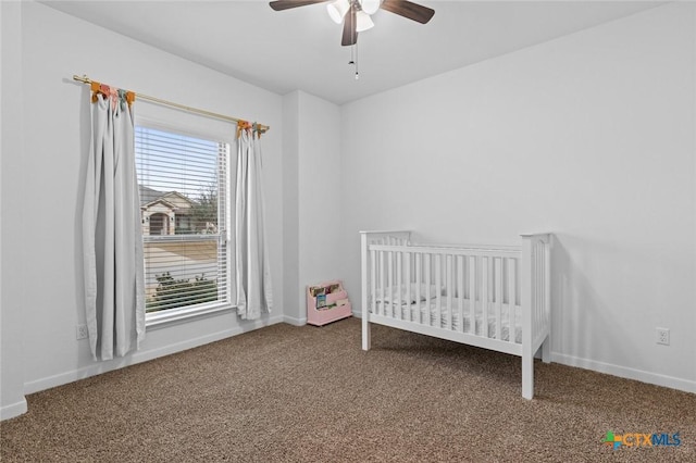 unfurnished bedroom featuring baseboards, a crib, a ceiling fan, and carpet flooring