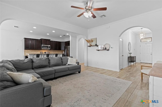 living area with arched walkways, visible vents, a ceiling fan, and ornamental molding