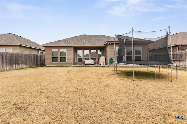 rear view of property with a trampoline, roof with shingles, a lawn, a fenced backyard, and a patio area