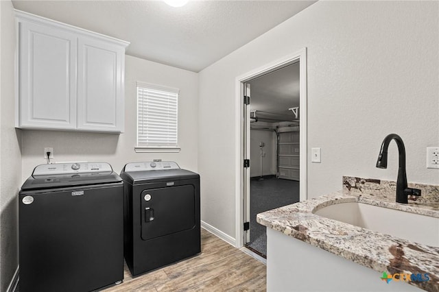 laundry area featuring sink, cabinets, a textured ceiling, light wood-type flooring, and independent washer and dryer