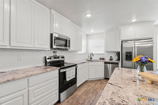 kitchen featuring white cabinetry, sink, backsplash, stainless steel appliances, and light wood-type flooring