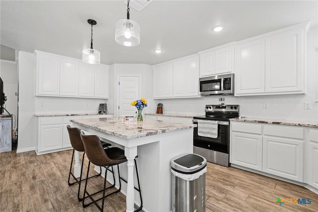 kitchen with appliances with stainless steel finishes, decorative light fixtures, white cabinets, a center island, and light hardwood / wood-style floors