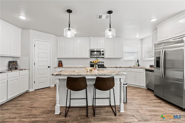 kitchen with sink, white cabinetry, a kitchen island, stainless steel appliances, and light stone countertops