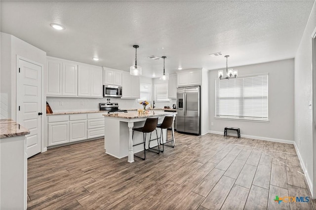 kitchen with light stone counters, light hardwood / wood-style flooring, appliances with stainless steel finishes, pendant lighting, and white cabinets