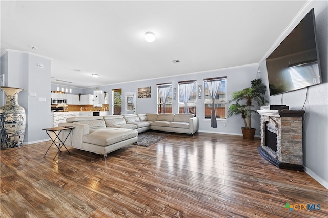 living room with dark wood-type flooring, ornamental molding, and a stone fireplace