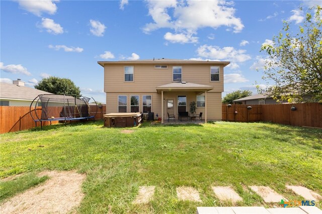 back of house with a patio, a lawn, a hot tub, and a trampoline