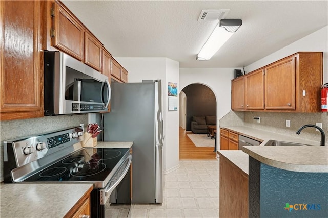2606 Wesley Dr, Killeen, TX 76549 - kitchen featuring stainless steel appliances, arched walkways, light floors, brown cabinets, and a textured ceiling