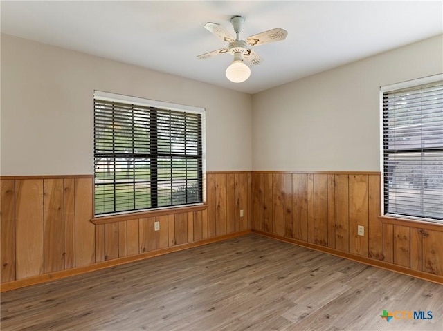 empty room with wood finished floors, a wainscoted wall, and a ceiling fan