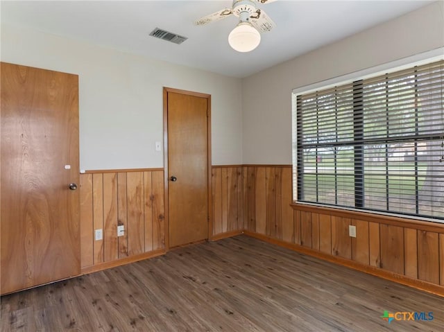 unfurnished room with a wainscoted wall, visible vents, wood finished floors, and ceiling fan