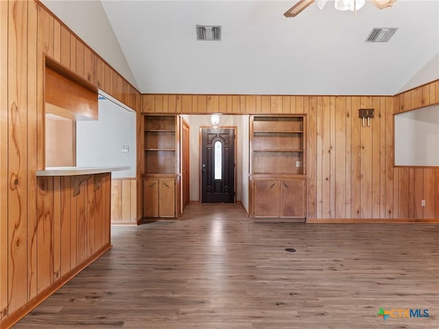 unfurnished living room featuring wood finished floors, wood walls, ceiling fan, visible vents, and lofted ceiling