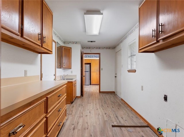 kitchen with freestanding refrigerator, light wood-style floors, brown cabinets, and a sink