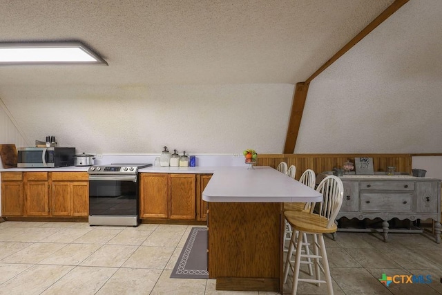 kitchen with kitchen peninsula, a textured ceiling, stainless steel appliances, light tile patterned floors, and a breakfast bar