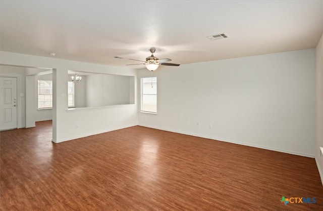 spare room with dark wood-type flooring, a healthy amount of sunlight, and ceiling fan with notable chandelier