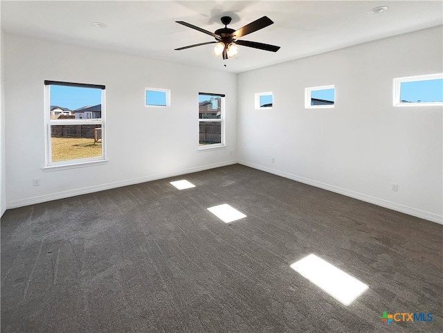 spare room with a wealth of natural light, ceiling fan, and dark colored carpet