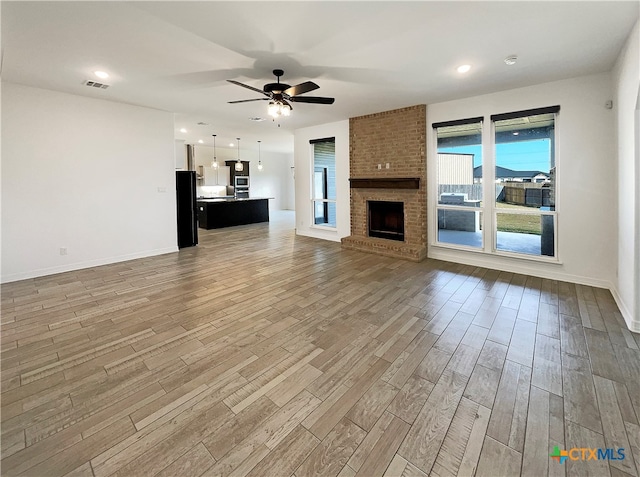 unfurnished living room with a brick fireplace, wood-type flooring, and ceiling fan