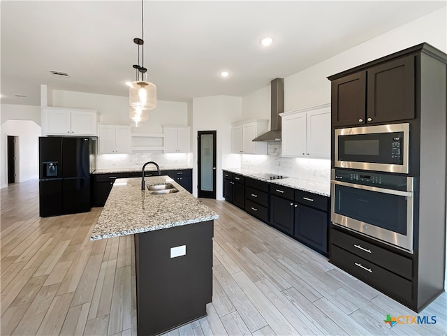 kitchen featuring black appliances, wall chimney range hood, white cabinets, and a kitchen island with sink