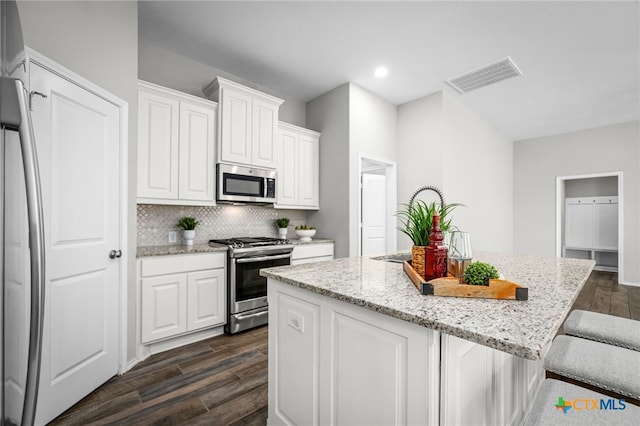 kitchen with light stone counters, visible vents, a kitchen island, dark wood-type flooring, and appliances with stainless steel finishes