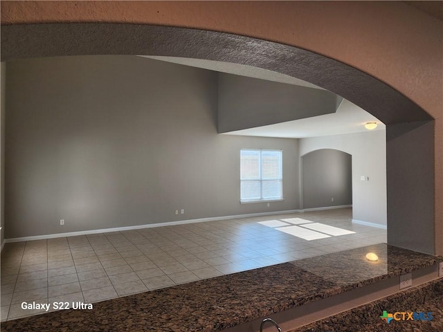 tiled spare room with arched walkways, vaulted ceiling, and baseboards