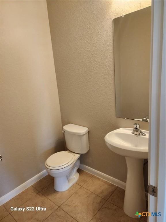 half bath featuring toilet, a textured wall, tile patterned floors, and baseboards
