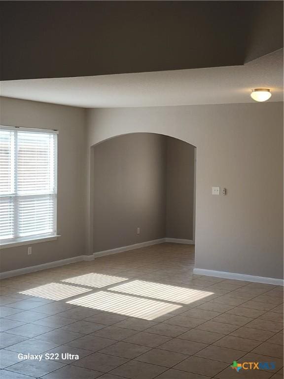 empty room with arched walkways, baseboards, and light tile patterned flooring