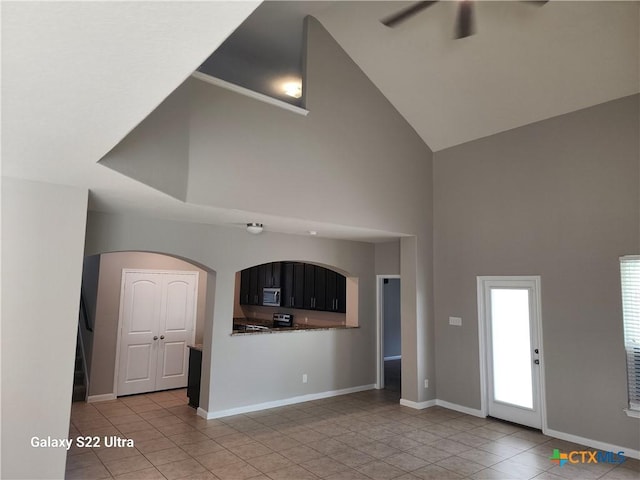 unfurnished living room featuring high vaulted ceiling, a ceiling fan, light tile patterned flooring, arched walkways, and baseboards