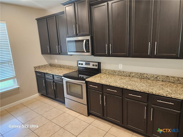 kitchen featuring baseboards, appliances with stainless steel finishes, light stone countertops, and light tile patterned floors