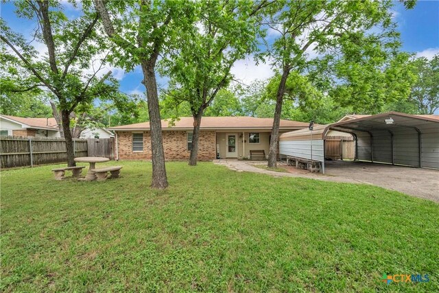 back of house with aphalt driveway, fence, brick siding, a yard, and a carport