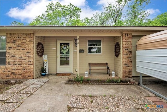 property entrance featuring a porch, a garage, and brick siding