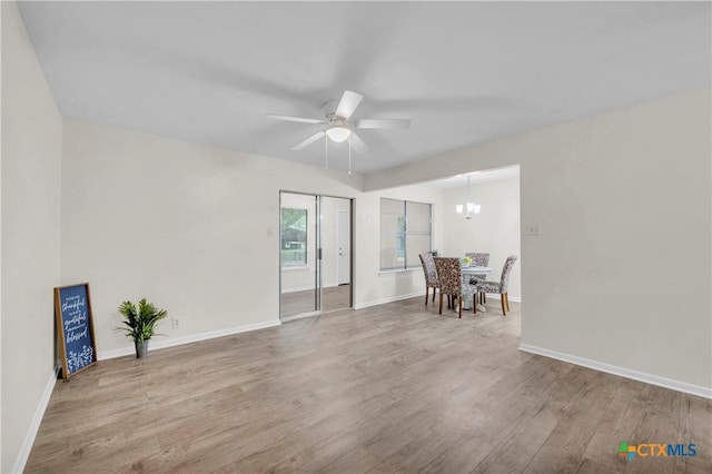 unfurnished room with baseboards, ceiling fan with notable chandelier, and wood finished floors