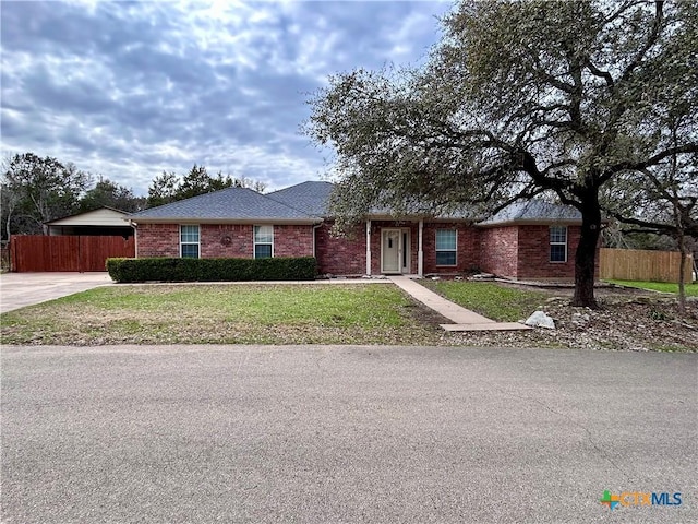 ranch-style home featuring brick siding, a front yard, fence, and a shingled roof