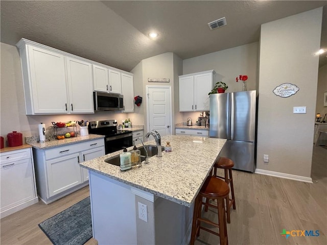 kitchen featuring white cabinetry, stainless steel appliances, light stone counters, a kitchen island with sink, and light wood-type flooring