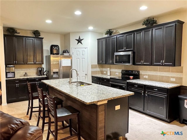 kitchen with light stone counters, a breakfast bar, stainless steel appliances, backsplash, and a sink