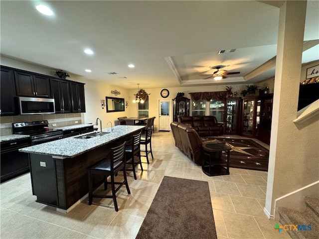 kitchen with appliances with stainless steel finishes, dark cabinets, light stone countertops, a kitchen bar, and a sink