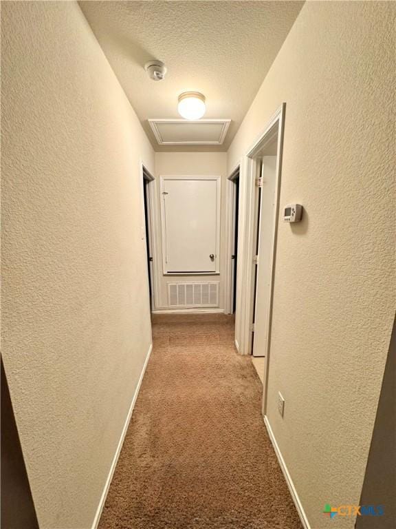 corridor featuring carpet, visible vents, a textured wall, attic access, and a textured ceiling