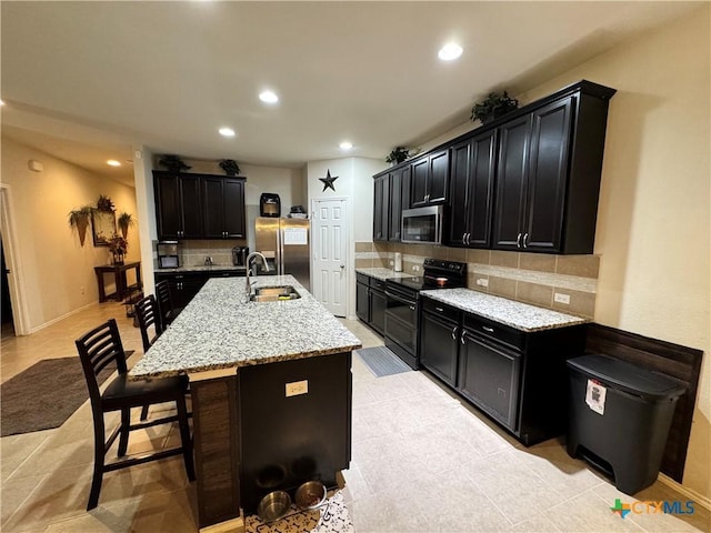 kitchen featuring tasteful backsplash, a breakfast bar, stainless steel appliances, dark cabinetry, and a sink