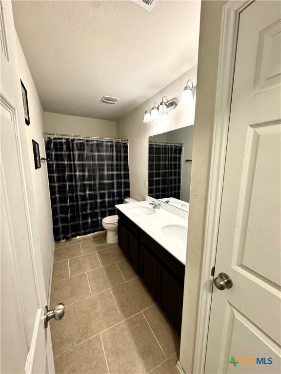 full bathroom featuring double vanity, toilet, tile patterned flooring, a textured ceiling, and a sink