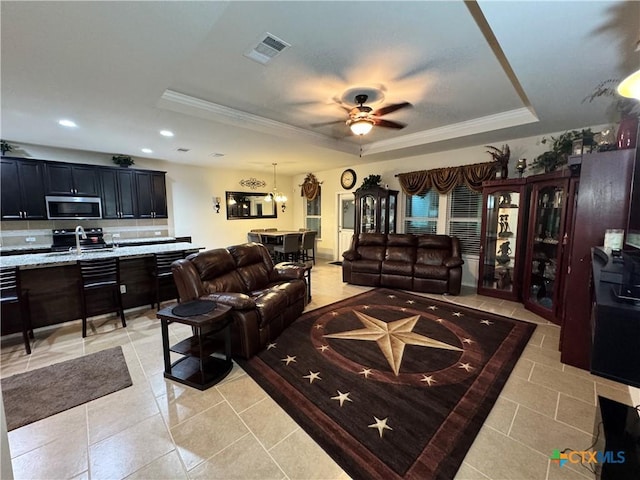 living area featuring a tray ceiling, crown molding, light tile patterned floors, visible vents, and ceiling fan